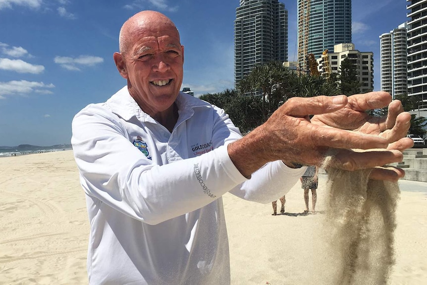 Lifeguard Warren Young with handfuls of sand on a Gold Coast beach.