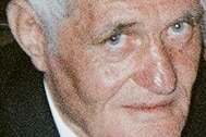 A headshot of an older man wearing suit with a flower in his lapel