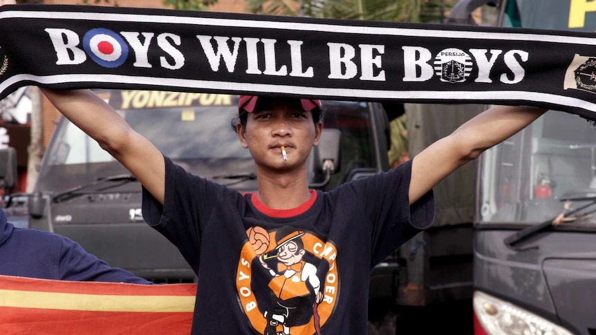 A Persija fan holds a banner reading: "Boys will be boys".