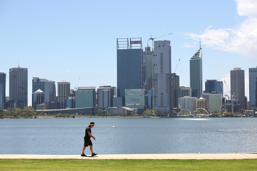 A man walks along a path on a sunny day with the Perth city skyline in the background.