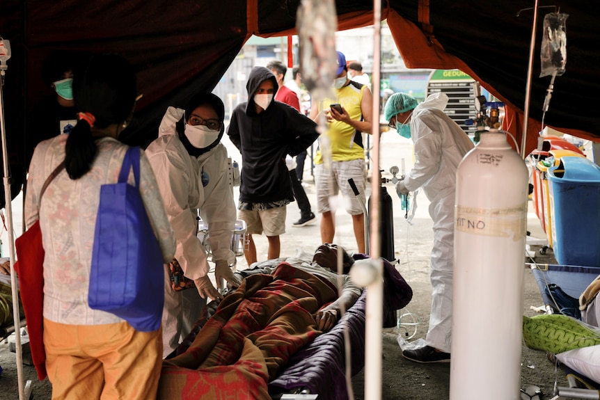 A group of medical workers dressed in protective gear and masks lean over a man hooked up to an oxygen tank.