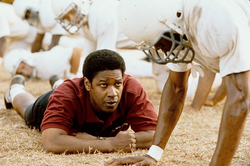 a film still from Remember the Titans showing Denzel Washington lying on the ground looking at a player in pads