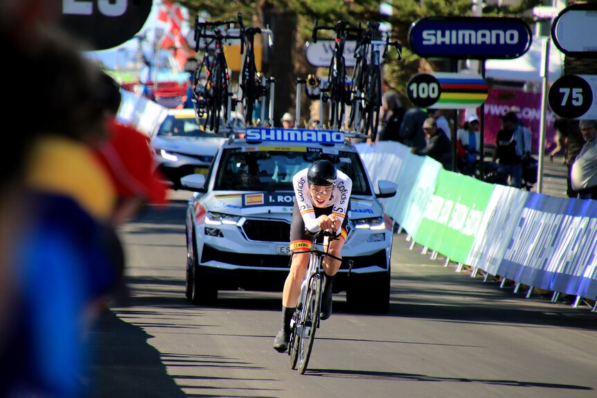 A cyclist rides along a road while being watched by spectators.