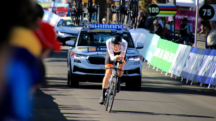 A cyclist rides along a road while being watched by spectators.