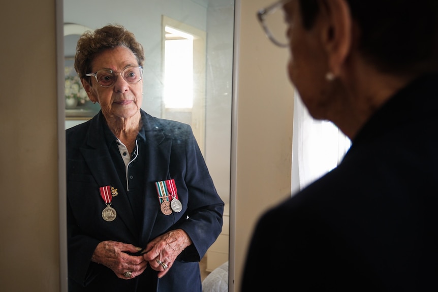 an older woman wearing war medals on her jacket looking at herself in the mirror