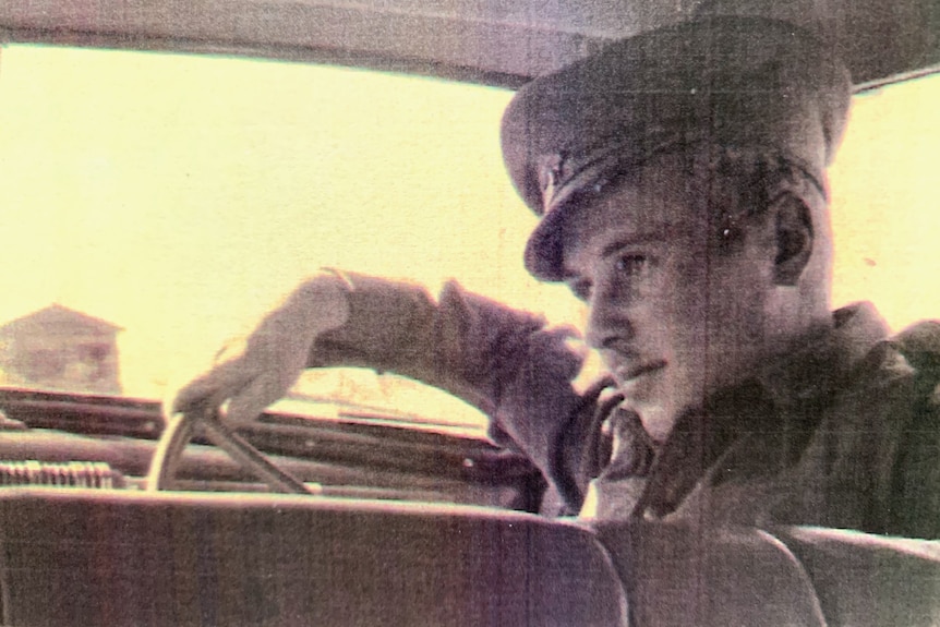 Black and white photograph of a young man in uniform at the wheel of a car.
