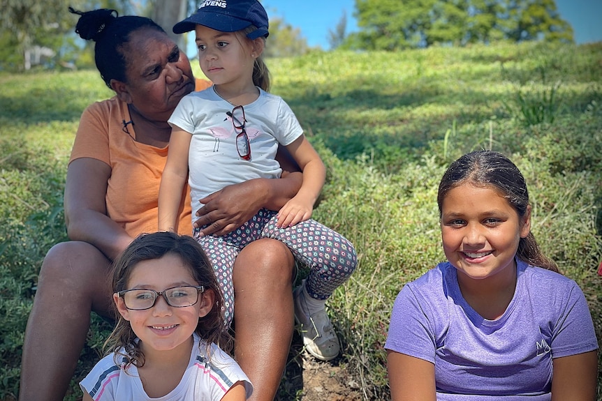 Belinda Boney sits with a grandchild on her lap and two grandchildren sit on the ground in front of her.