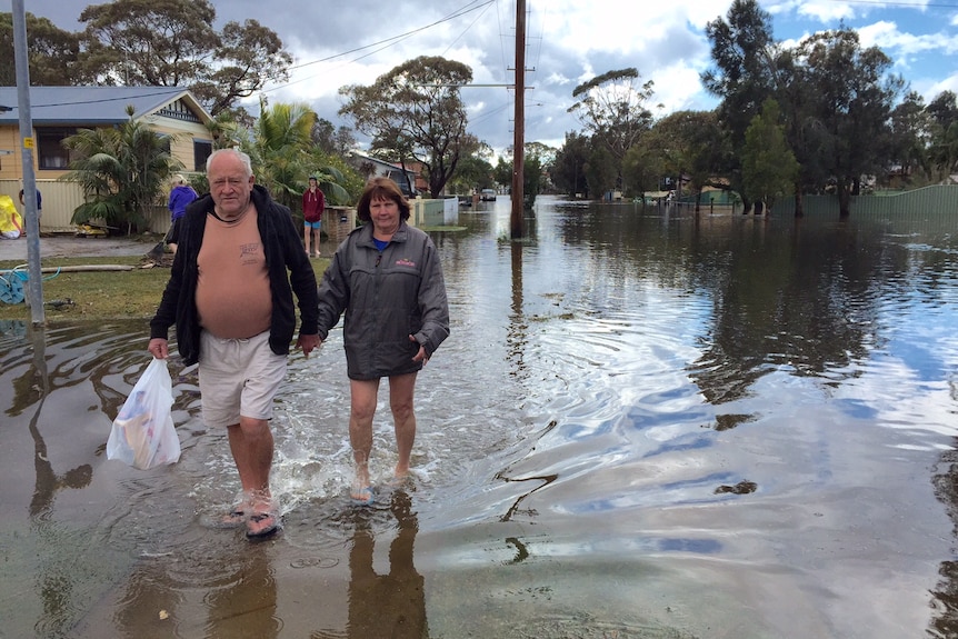 A couple walks through floodwater in Sussex Inlet, NSW