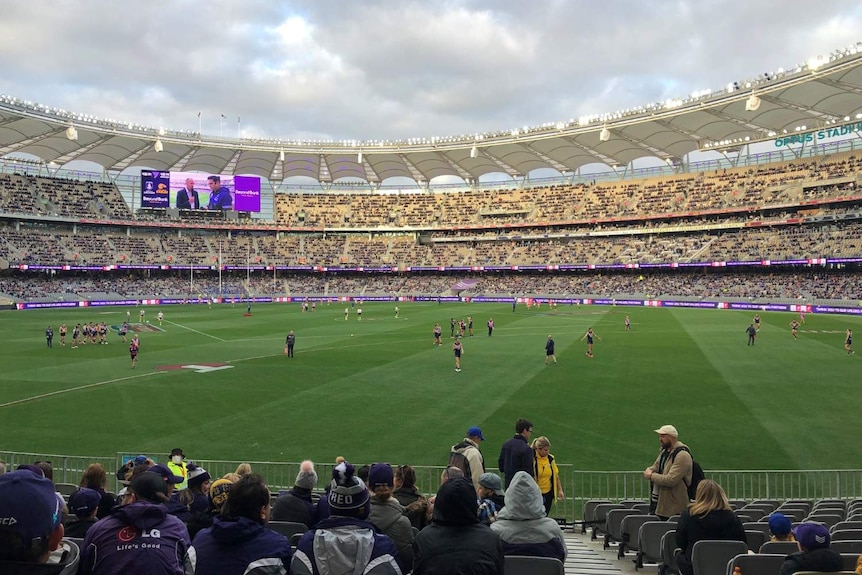Fans inside Perth Stadium before the Western Derby, with teams warming up on the field