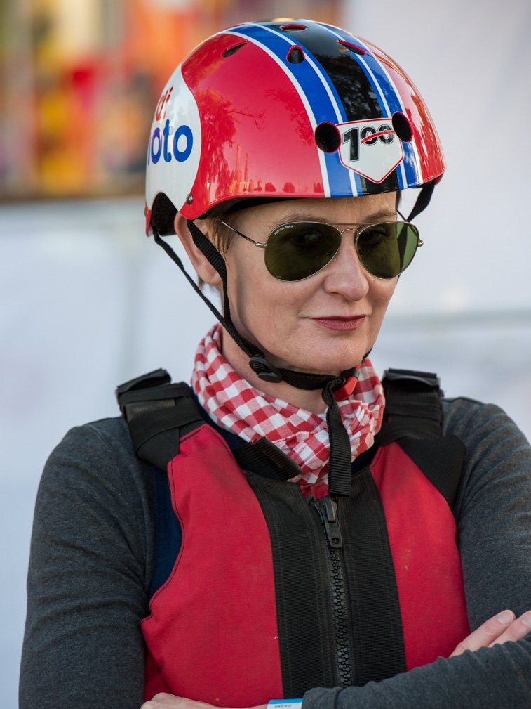 A woman wearing a helmet, buoyancy aid and sunglasses who is smiling