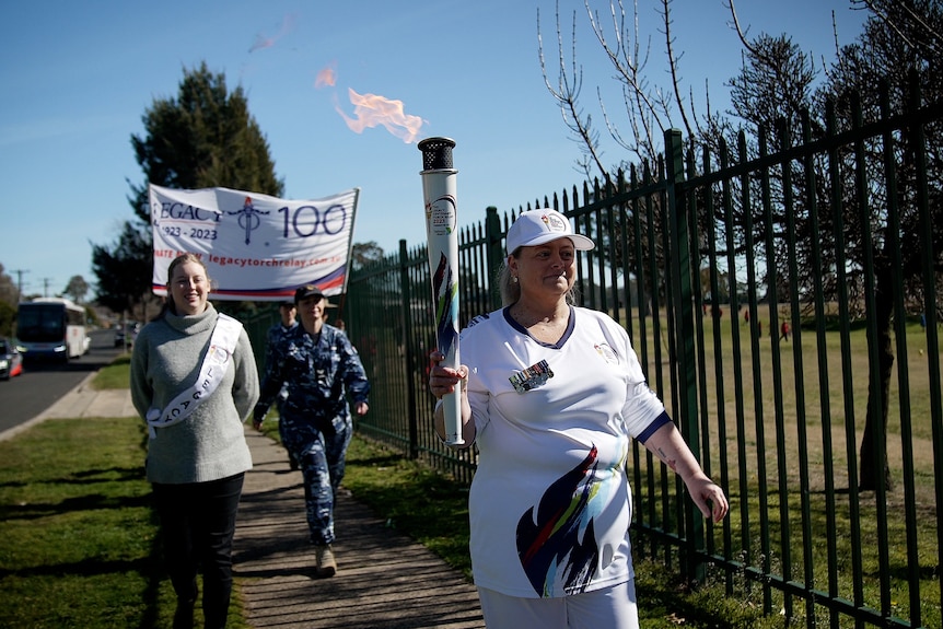 A woman jogging in running gear carries a lighted torch.