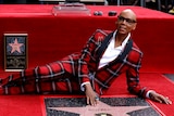 RuPaul in a red and black tartan suits lays next to a Hollywood star bearing his name