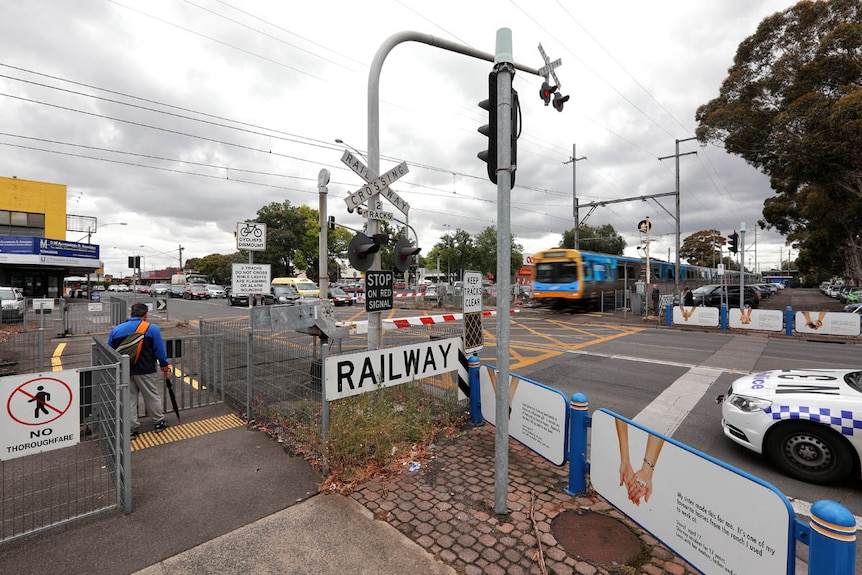 A pedestrian waits to cross the Glenroy level crossing, which is closed as a train moves past.