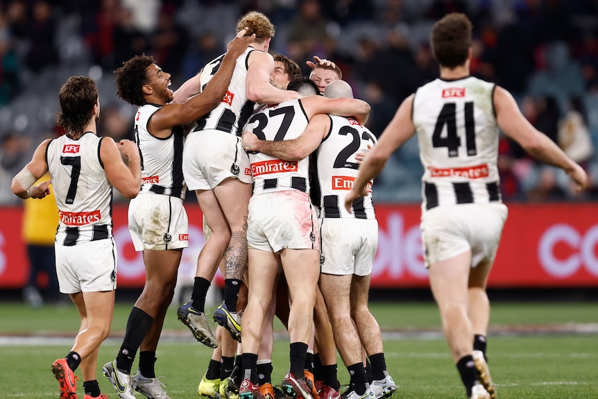A number of happy Collingwood AFL players have a group hug in the middle of the MCG after a game.