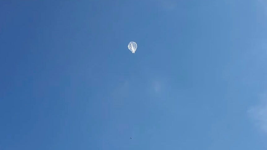 A clear balloon floats in blue sky. 