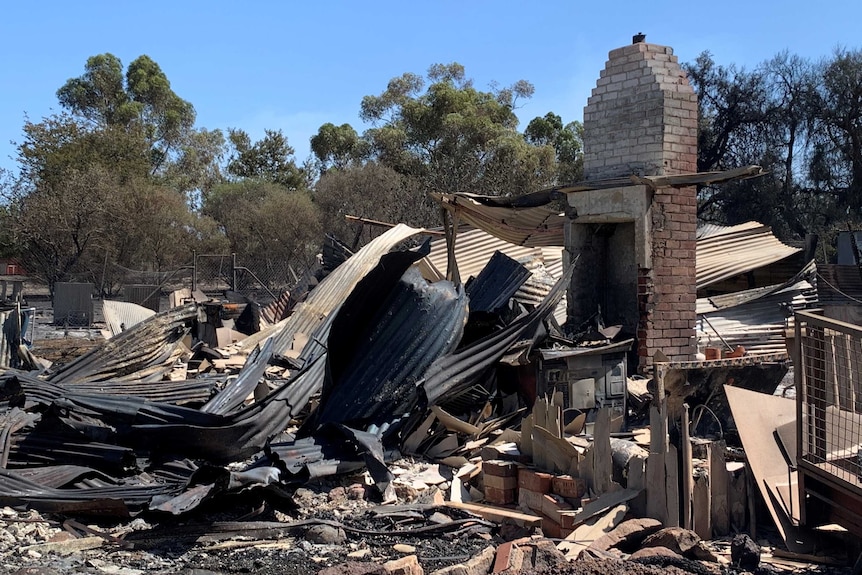 Twisted and burned corrugated metal sheets around a brick wall that remains standing.