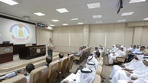 Major general Hindmarsh stands in front of a room of students wearing traditional UAE garb. They are all male.