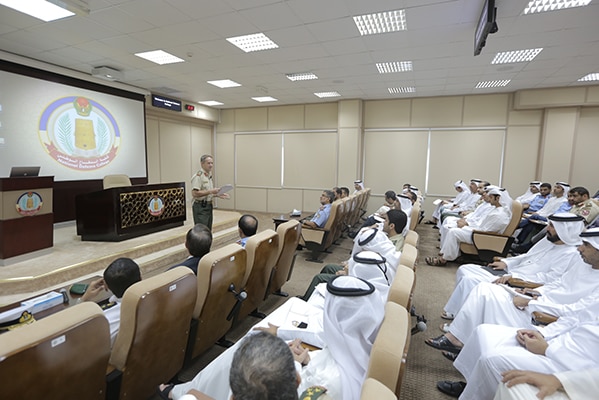 Major general Hindmarsh stands in front of a room of students wearing traditional UAE garb. They are all male.