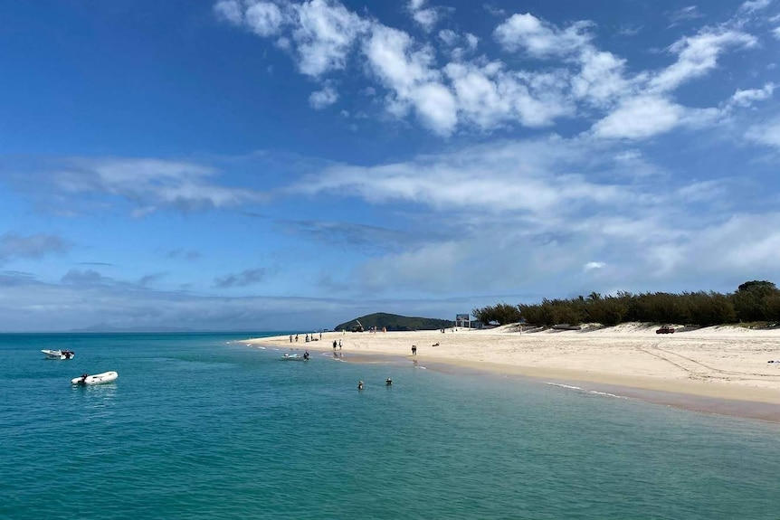 People swim in clear blue water surrounded by a white sand beach.