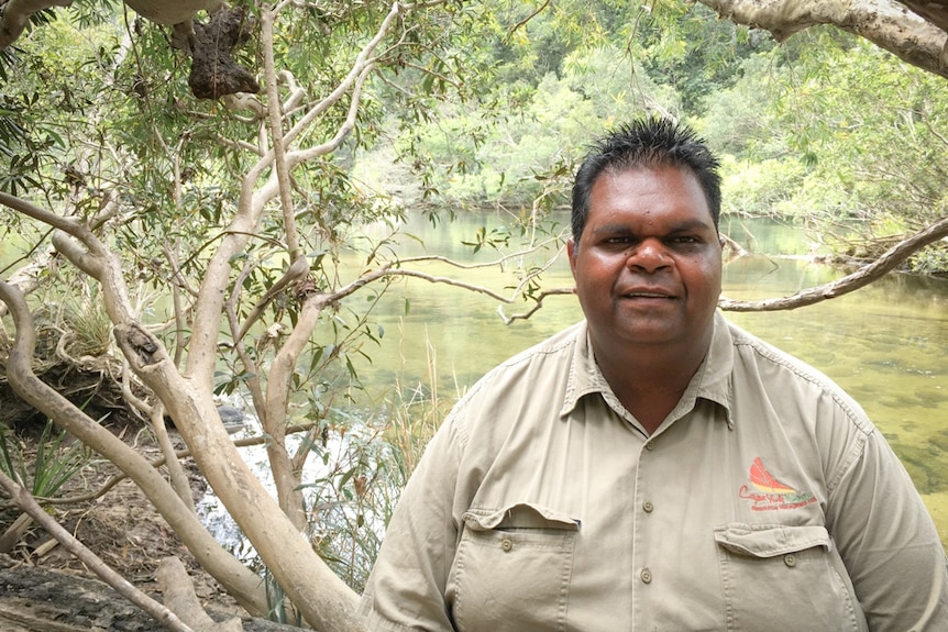 An Indigenous man in a council uniform sits by a river.