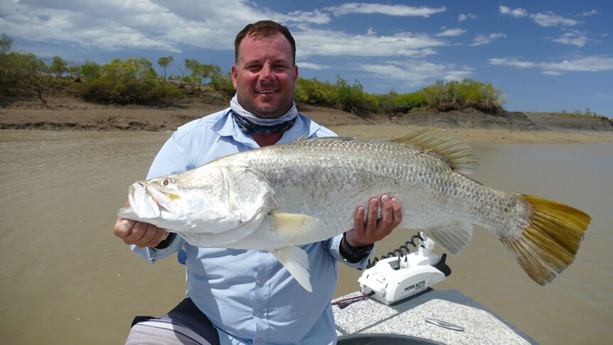 Man holding a tagged silver barramundi with yellow fins.