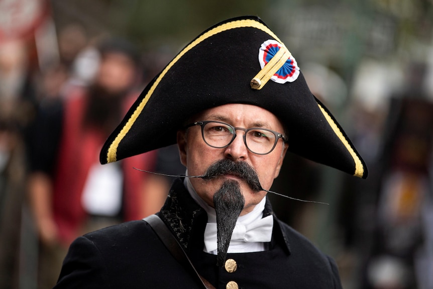A man with a black mostache and sharp spiky hairsprayed beard wearing a pirate hat 