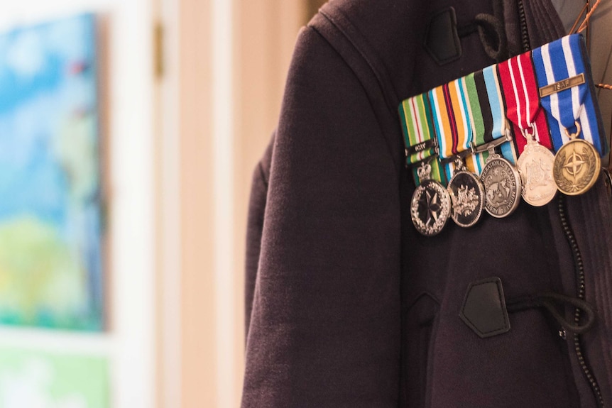 Four Army medals pinned to a child's jacket that is hanging on the back of a door.