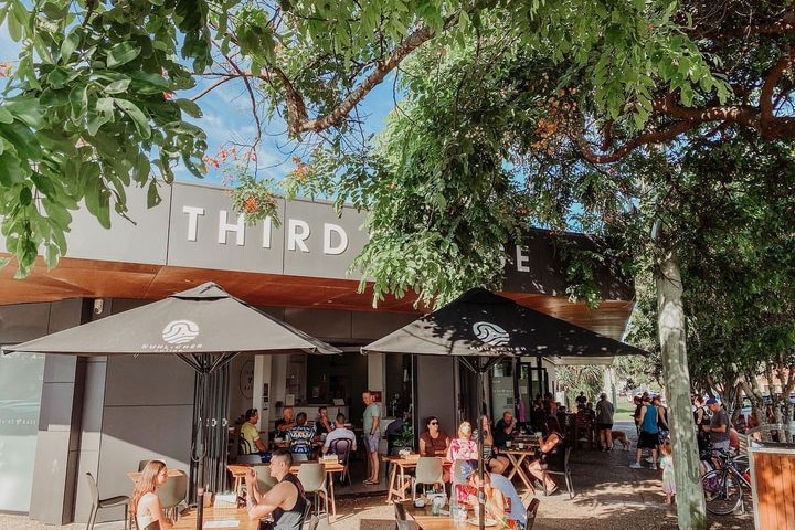 The outdoor area of a busy cafe with umbrellas, the awning reads 'THIRD BASE' 