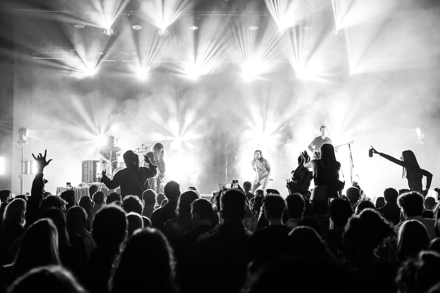 A crowd watches a band perform on a stage with bright lights behind it