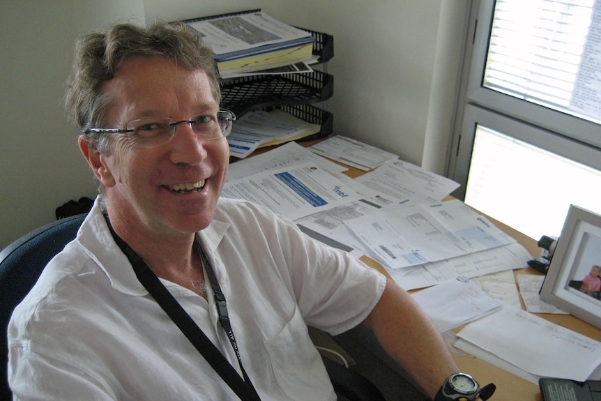 Dr Drew Wenck smiles as he sits at a desk.