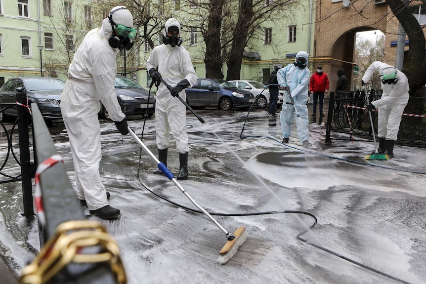 People in white suits and gas masks use brooms and spray detergent on a street in Moscow.