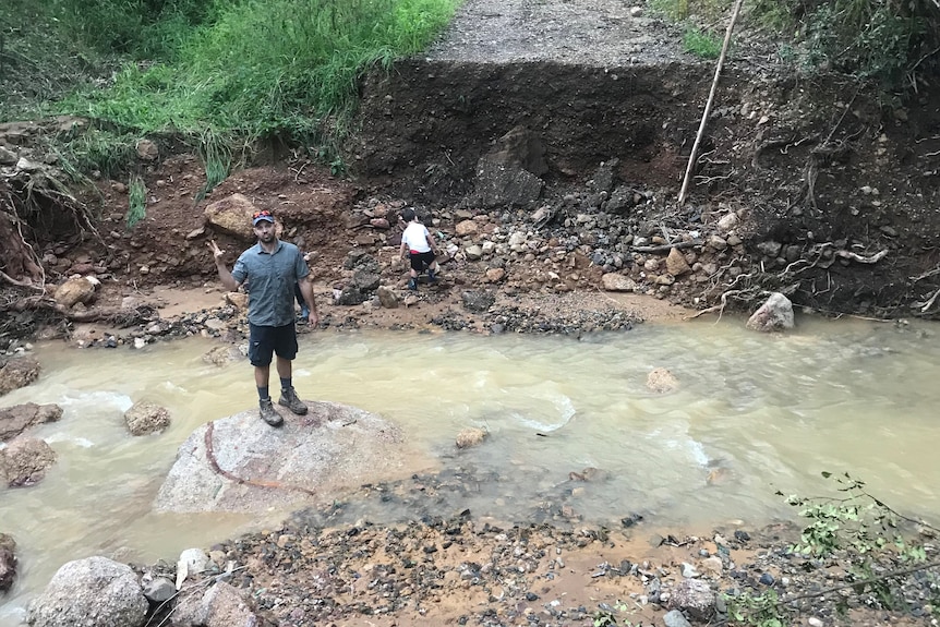 A man stands in a creek, in the middle of a washed out road.