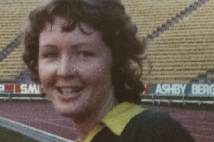 Sue Monteath smiles at the camera wearing a green football jersey