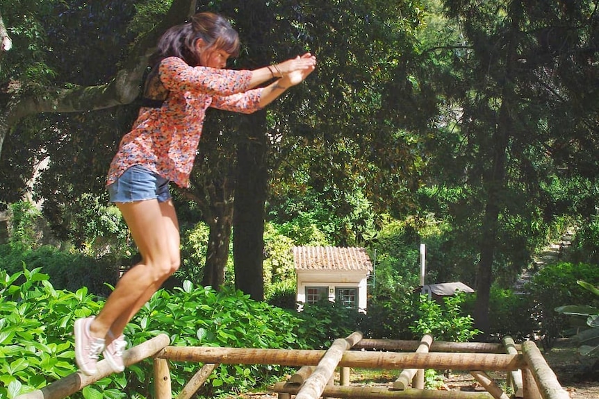 Amy Han does parkour on some wooden poles in a park