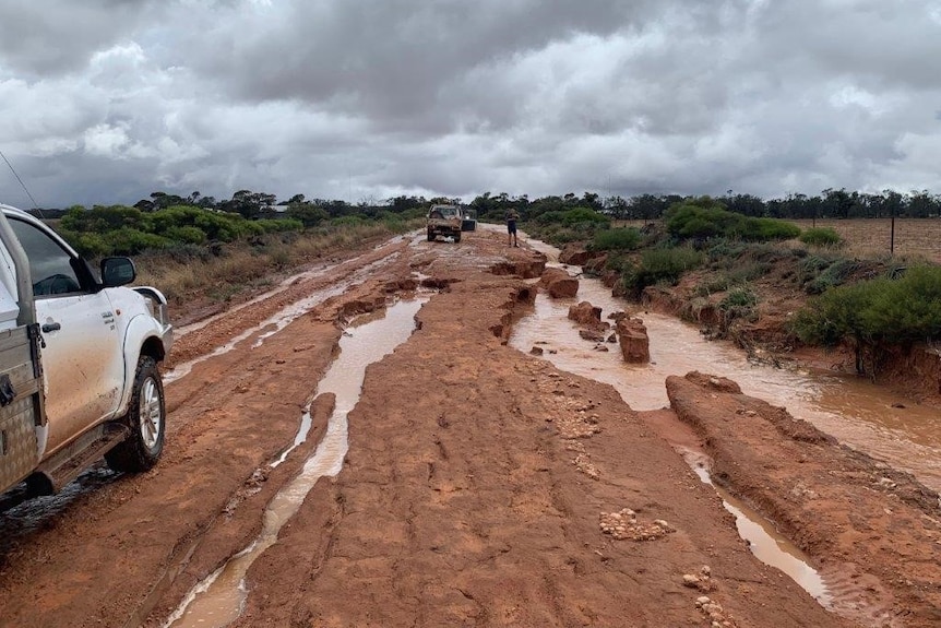 Cars on dirt road with big puddles gauged out of road surface.