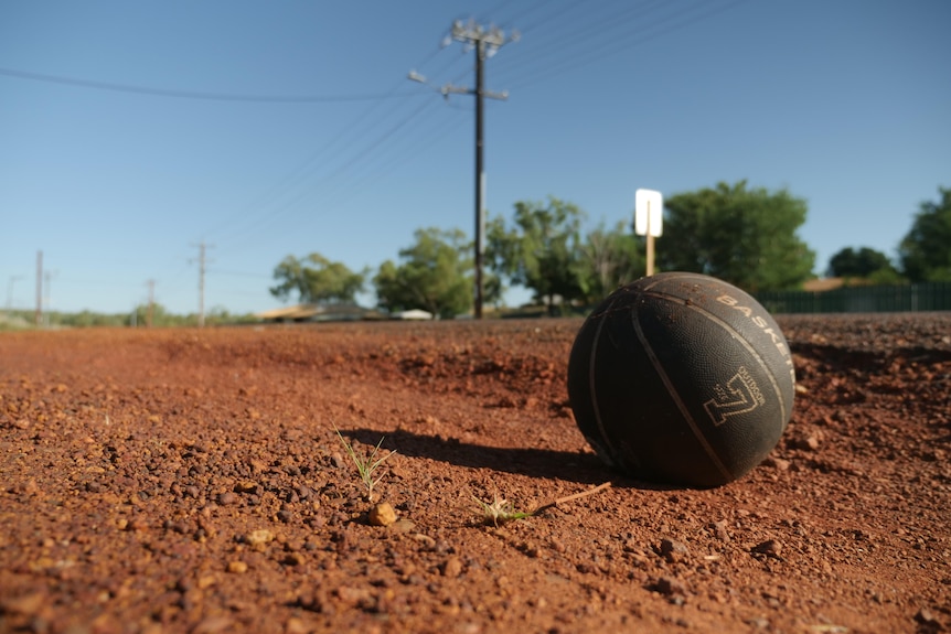 A basketball sits on a dirt path along a street
