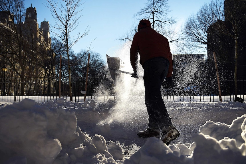 A man cleans the sidewalk of snow along Columbus Avenue in New York.