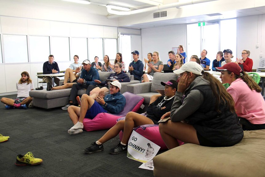 Players, coaches and staff at the National Tennis Academy clapping for John Millman as they watch the match on television.