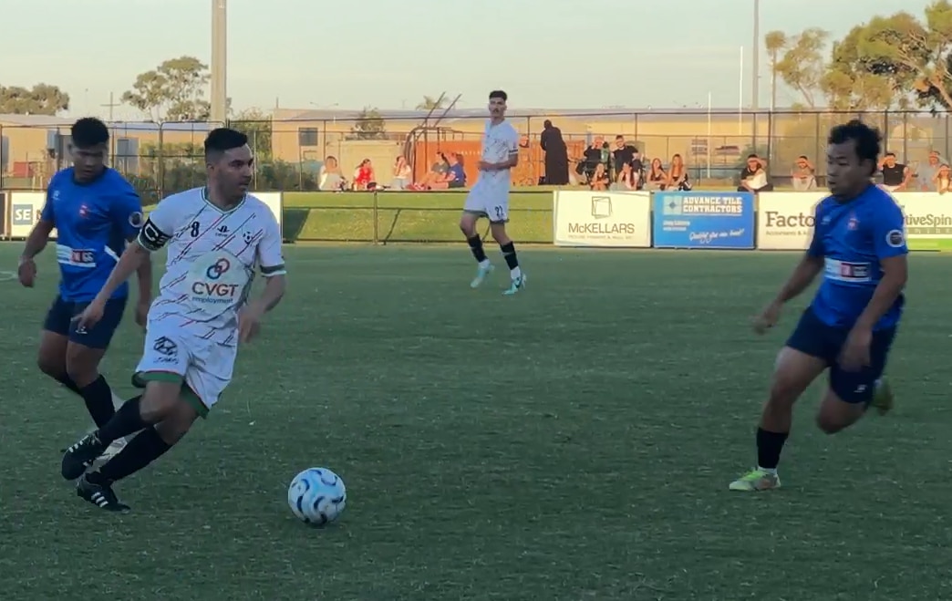 A man playing a soccer match with the ball right in front of him and several opposing players near him