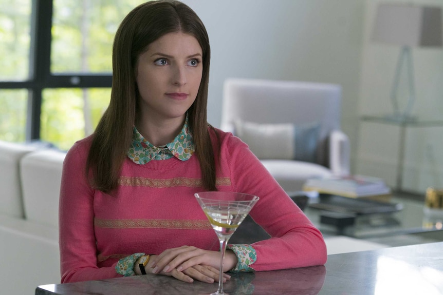Colour still of Anna Kendrick wearing a pink sweater sitting at a bench with a martini class in 2018 film A Simple Favour.