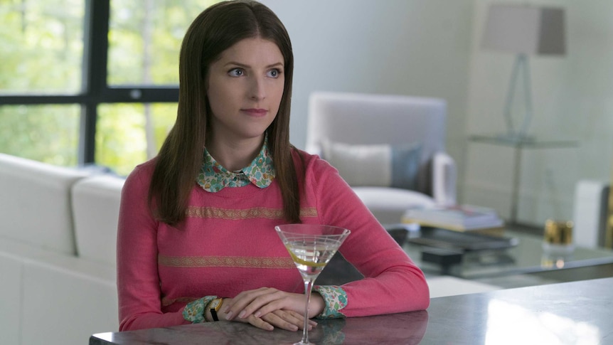 Colour still of Anna Kendrick wearing a pink sweater sitting at a bench with a martini class in 2018 film A Simple Favour.