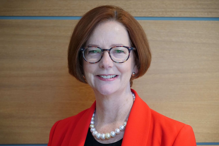 Julia Gillard poses for a photo in front of a brown-coloured wall