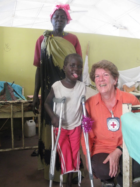 A small African child on crutches next to a woman in an orange shirt kneeling down smiling.