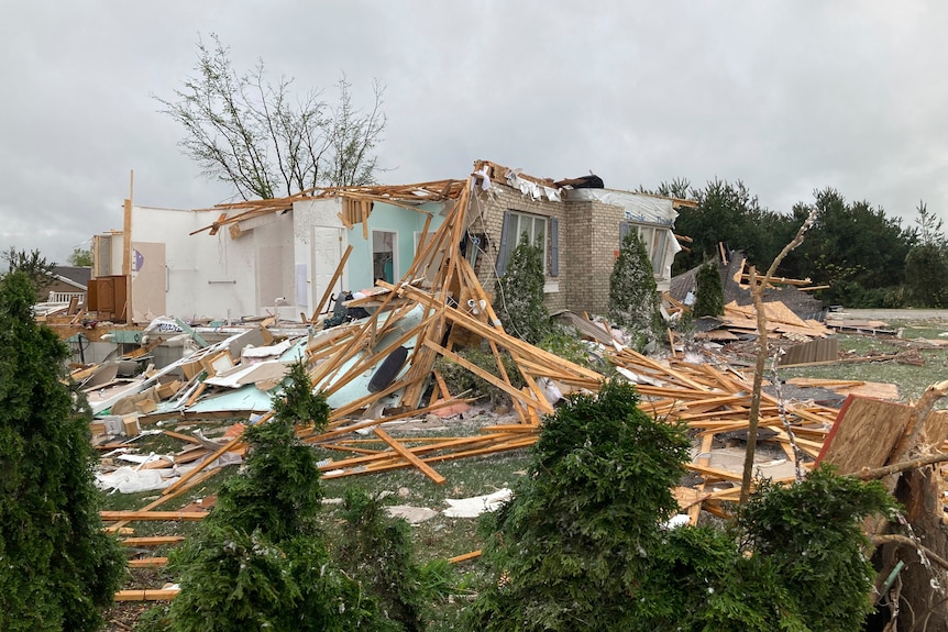 part of a home is broken into pieces with wood beams scattered around the yard outside