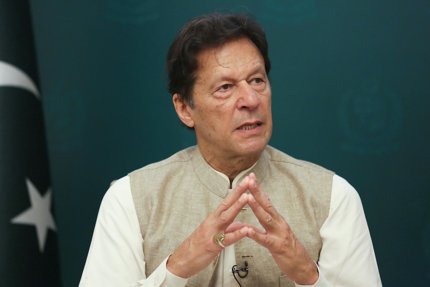Imran Khan wearing white with his hands forming a triangle. 