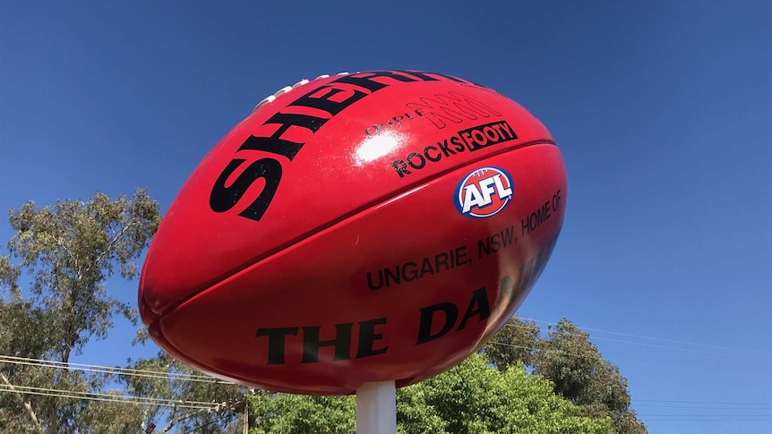 A massive Sherrin football on a large white post with blue sky in background