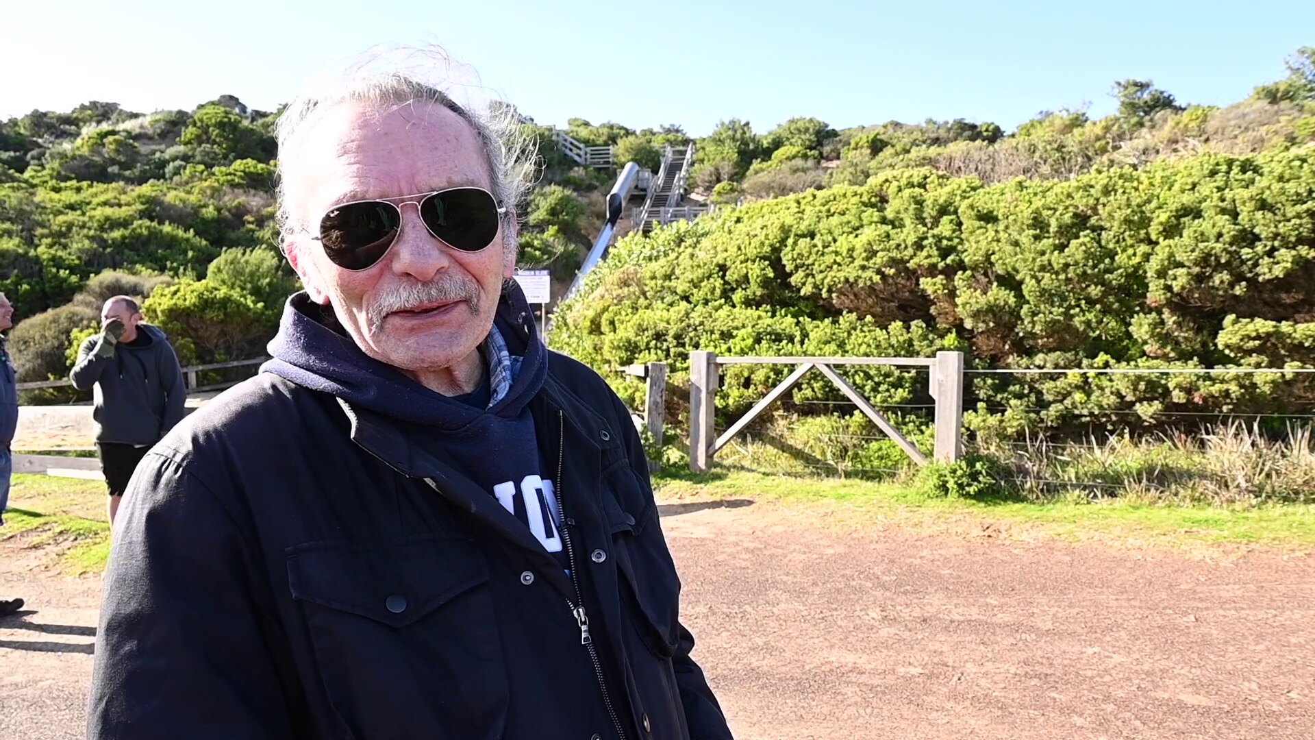 Portrait of a man wearing dark sunglasses with green coastal shrubs behind
