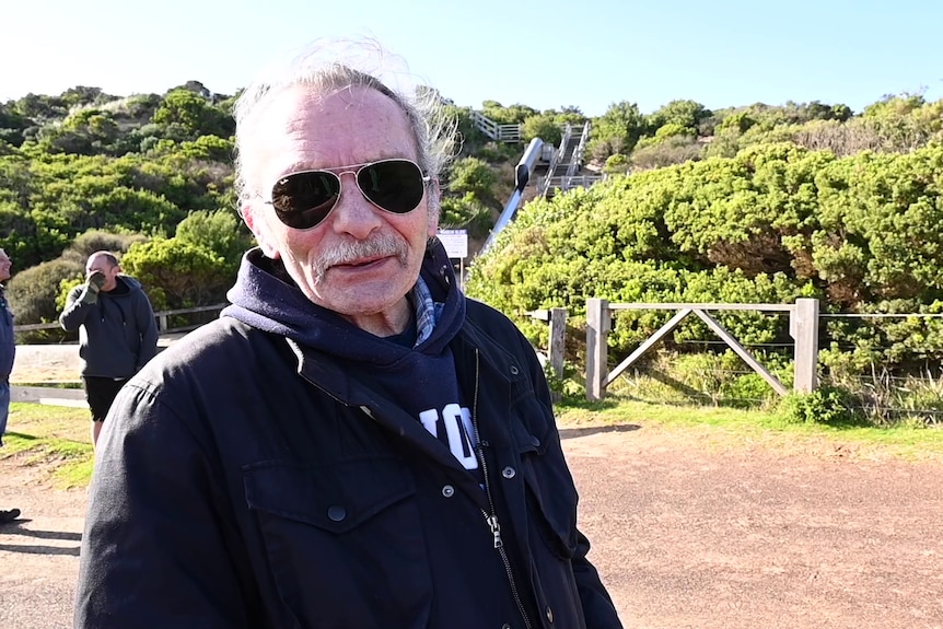 Portrait of a man wearing dark sunglasses with green coastal shrubs behind