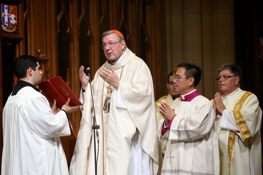 Man in white religious robe with red cap reading out sermon with others praying