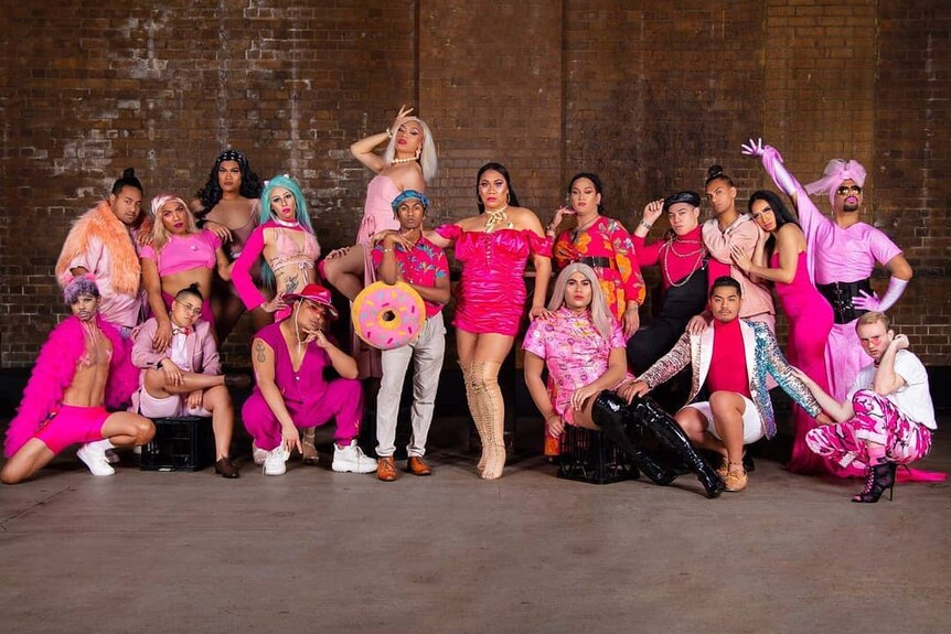 Eighteen members of Runway Movement pose for a stylised group photo, all wearing bright prink.